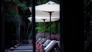 A row of lounge chairs with a large umbrella, a staircase, and lush greenery in the background. - Golden Temple Villa (Siem Reap)