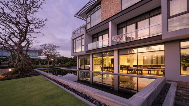 A modern building with large windows, a rooftop terrace, and a landscaped garden with a water feature. - Montgomerie Links Hotel & Villas (Da Nang)