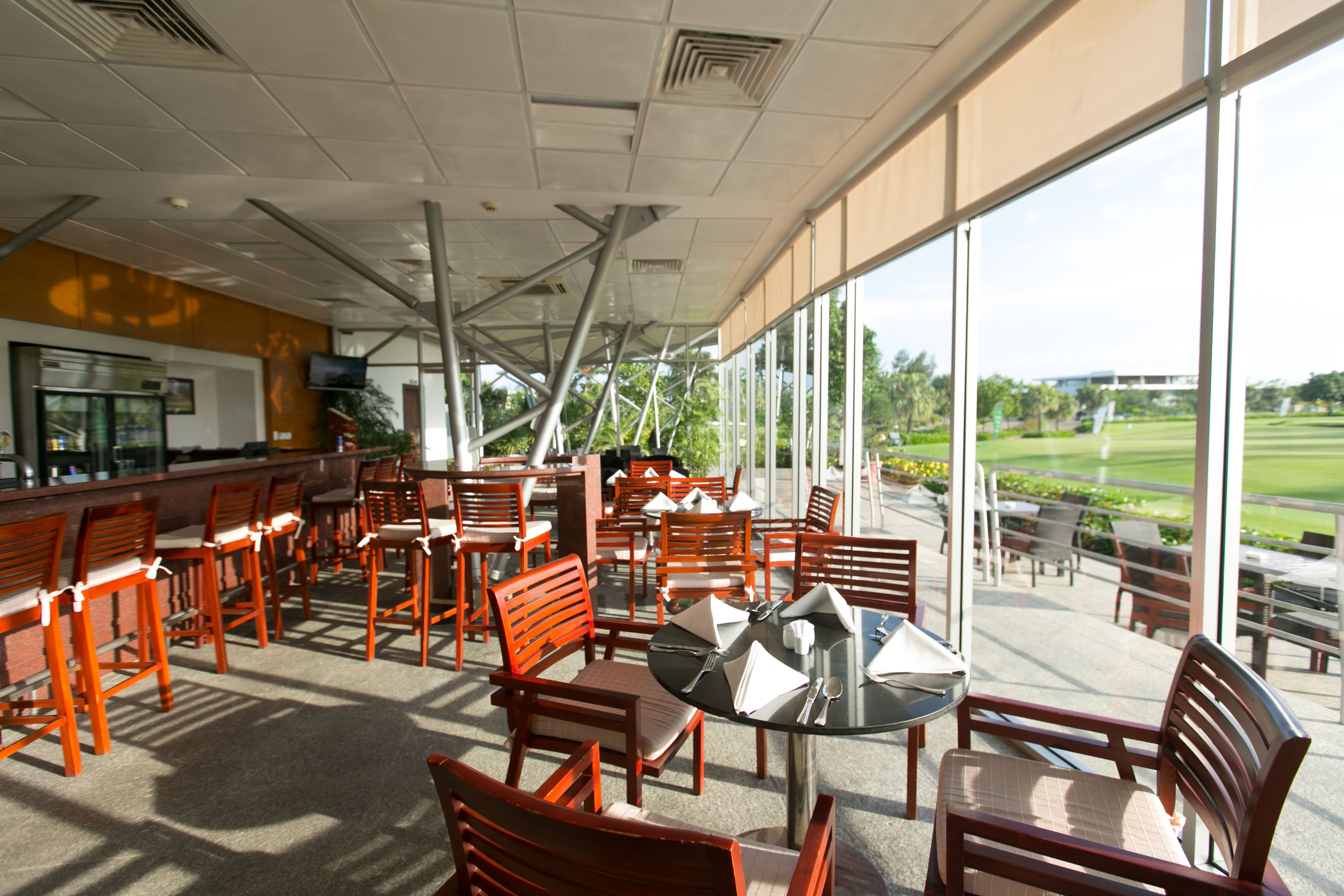 An outdoor seating area with wooden chairs and tables, large windows offering a view of a golf course.