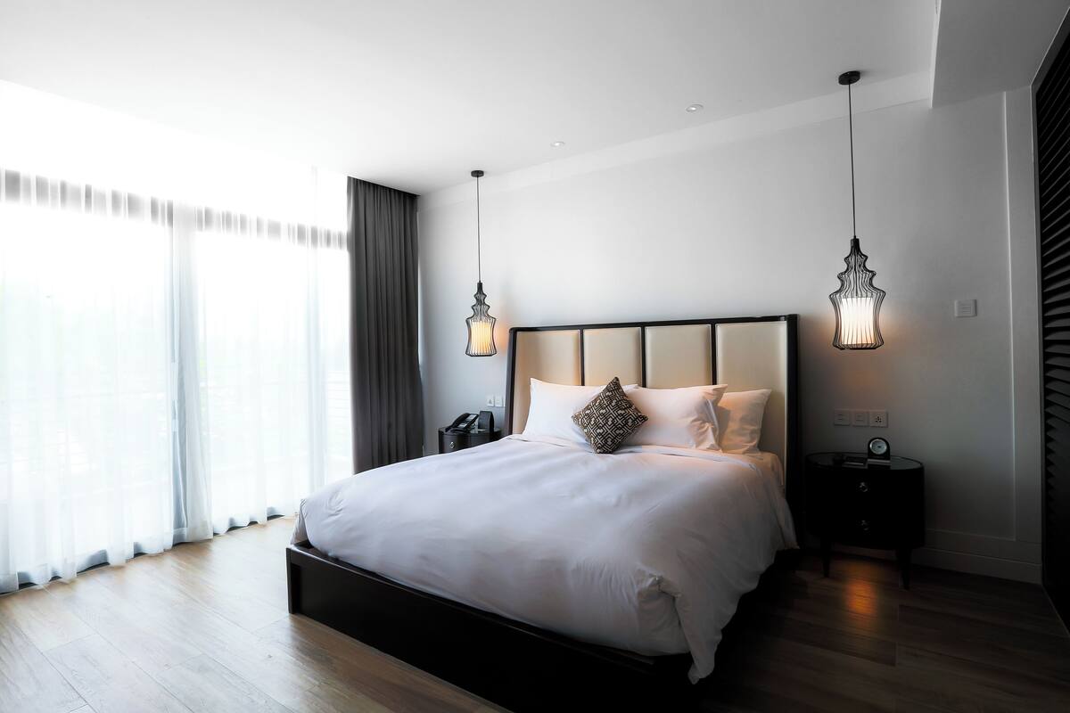 Moderni hotellihuone, jossa on suuri sänky, yöpöydät ja suuri ikkuna, jossa on verhot.