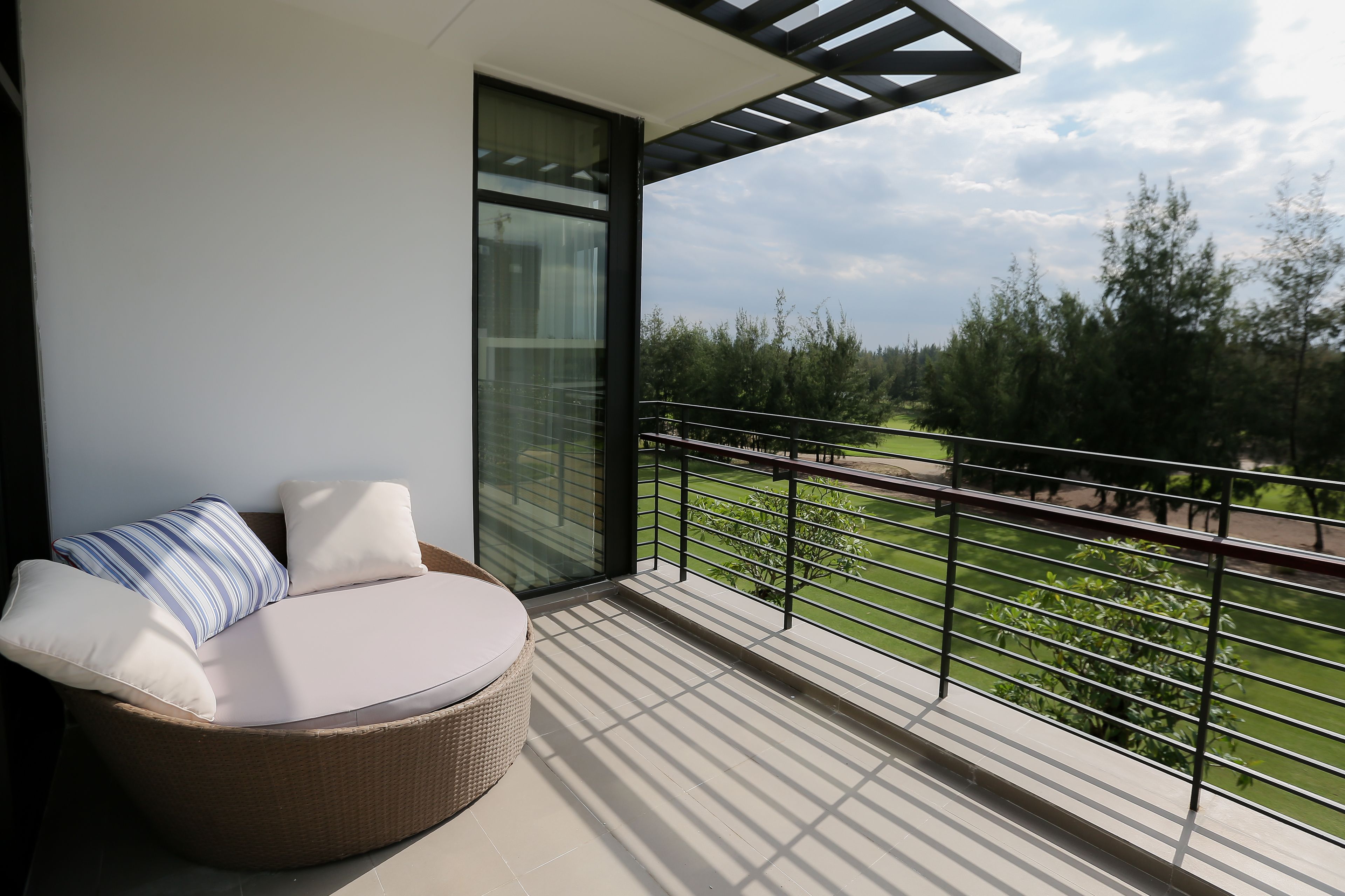 A balcony with a wicker sofa, a glass door, and a view of a green landscape.