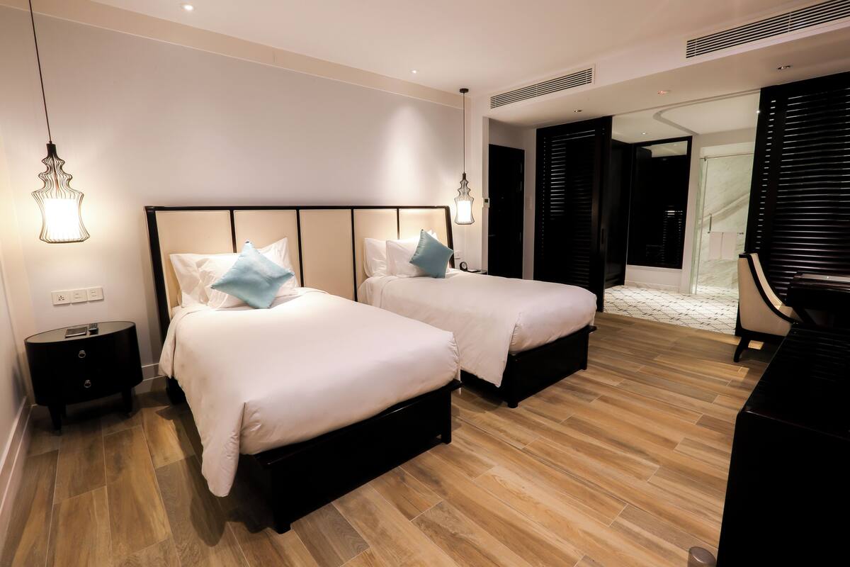 Hotellihuone, jossa on kaksi sänkyä, musta yöpöytä, musta työpöytä ja musta tuoli.
