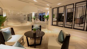 A modern lobby with a reception desk, seating area, and a staircase leading to upper floors. - Montgomerie Links Hotel & Villas (Da Nang)