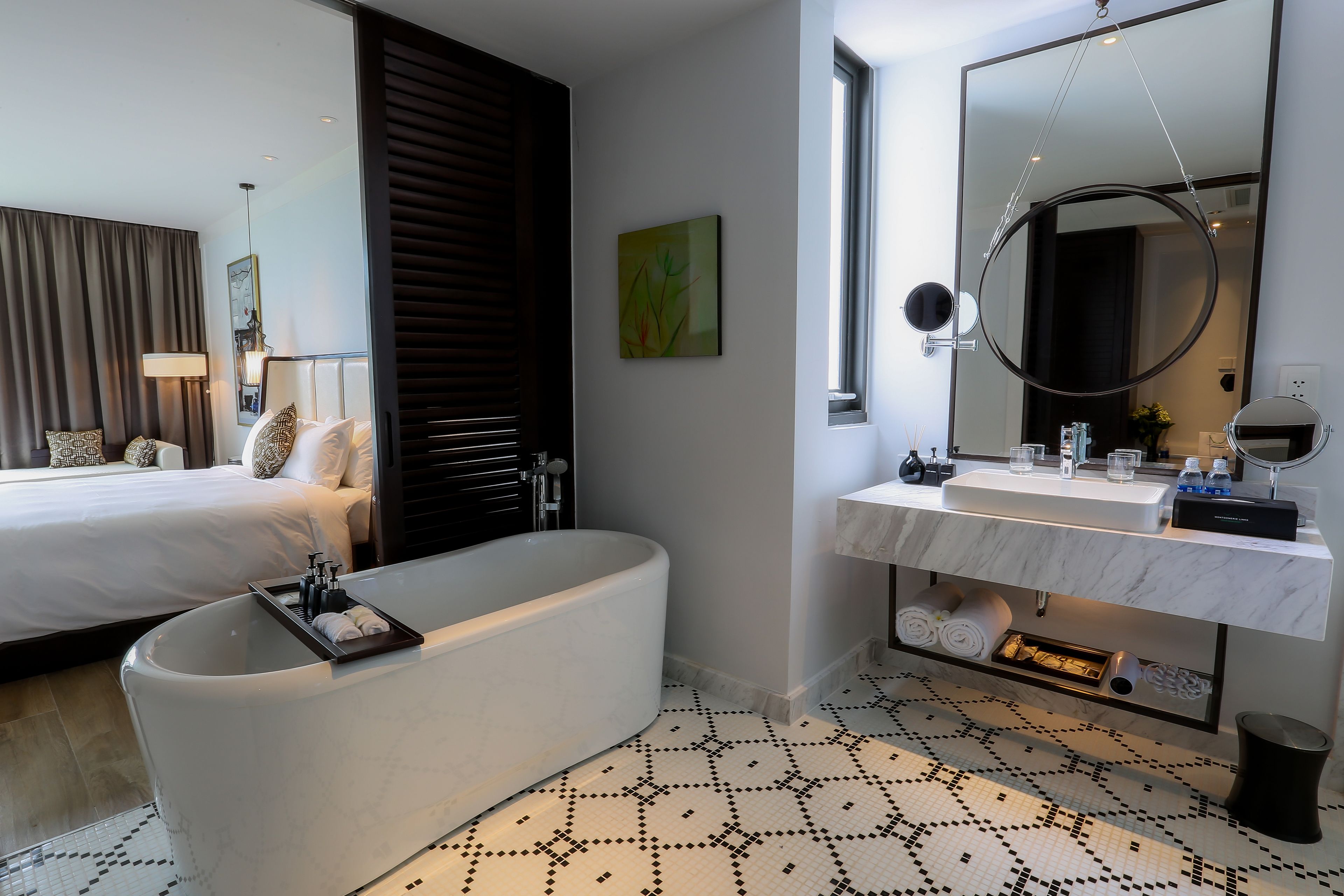 Een moderne hotelkamer met een groot bed, een badkuip, een badkamer met een marmeren wastafel en een grote spiegel.