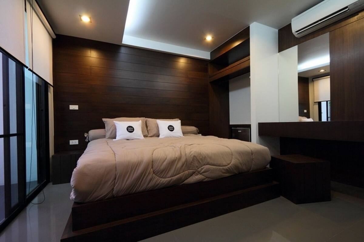 A modern bedroom with a large bed, dark wood paneling, a built-in bench, and a large window.