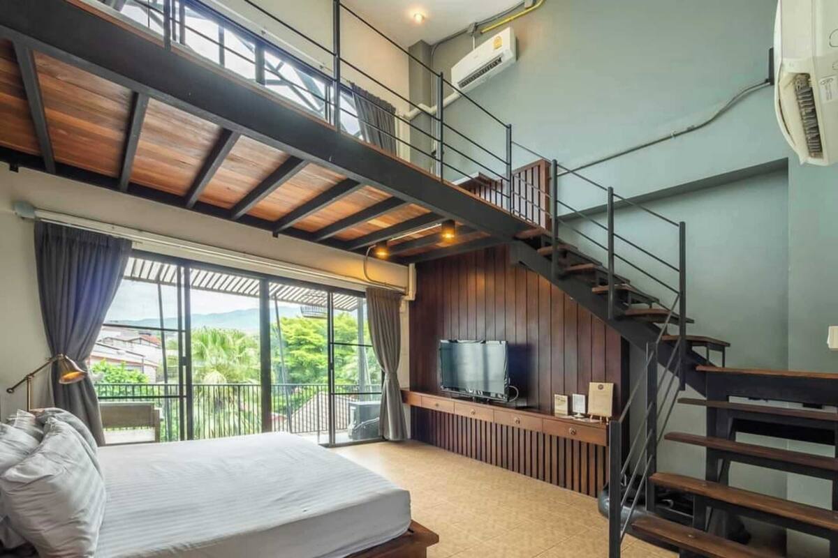 A bedroom with a large bed, a TV, a balcony, and a staircase.