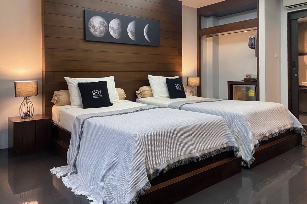A modern hotel room with two beds, wooden paneling on the walls, a large moon phase painting, and a minibar.
