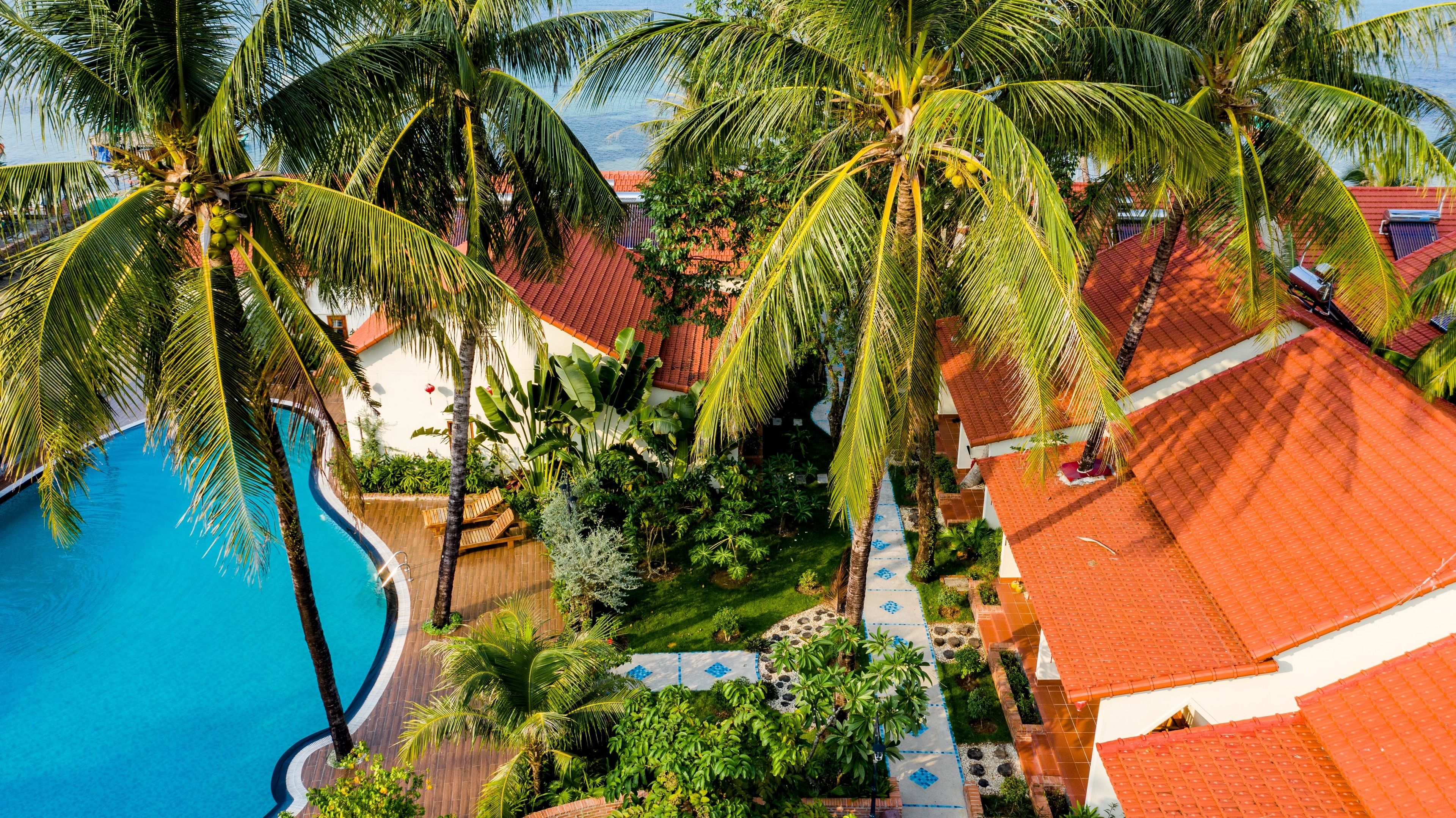Un resort con piscina, palme e un edificio con tetto rosso.