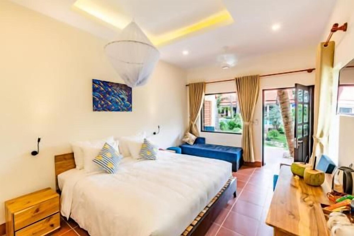 Un dormitorio con cama, mesitas de noche, ventana con cortinas y vistas a zonas verdes.