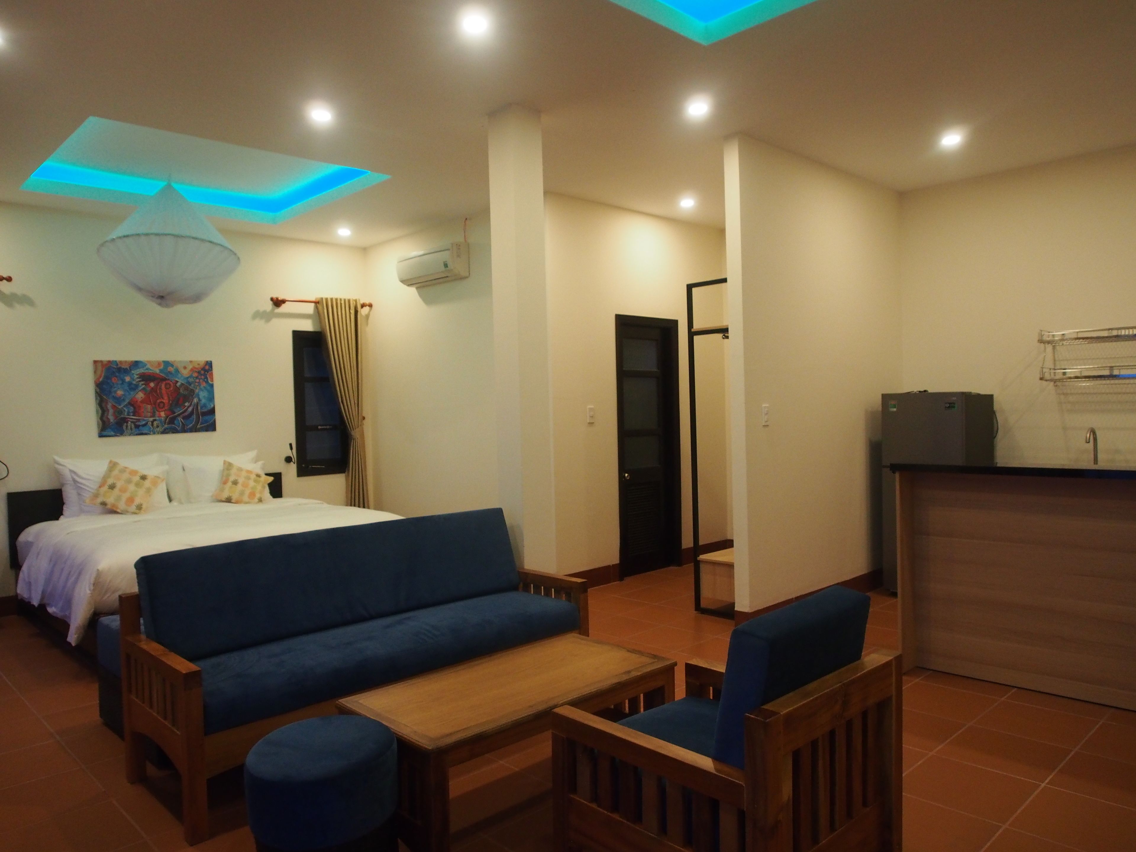 A hotel room with a bed, a sofa, a small table, and a kitchenette.