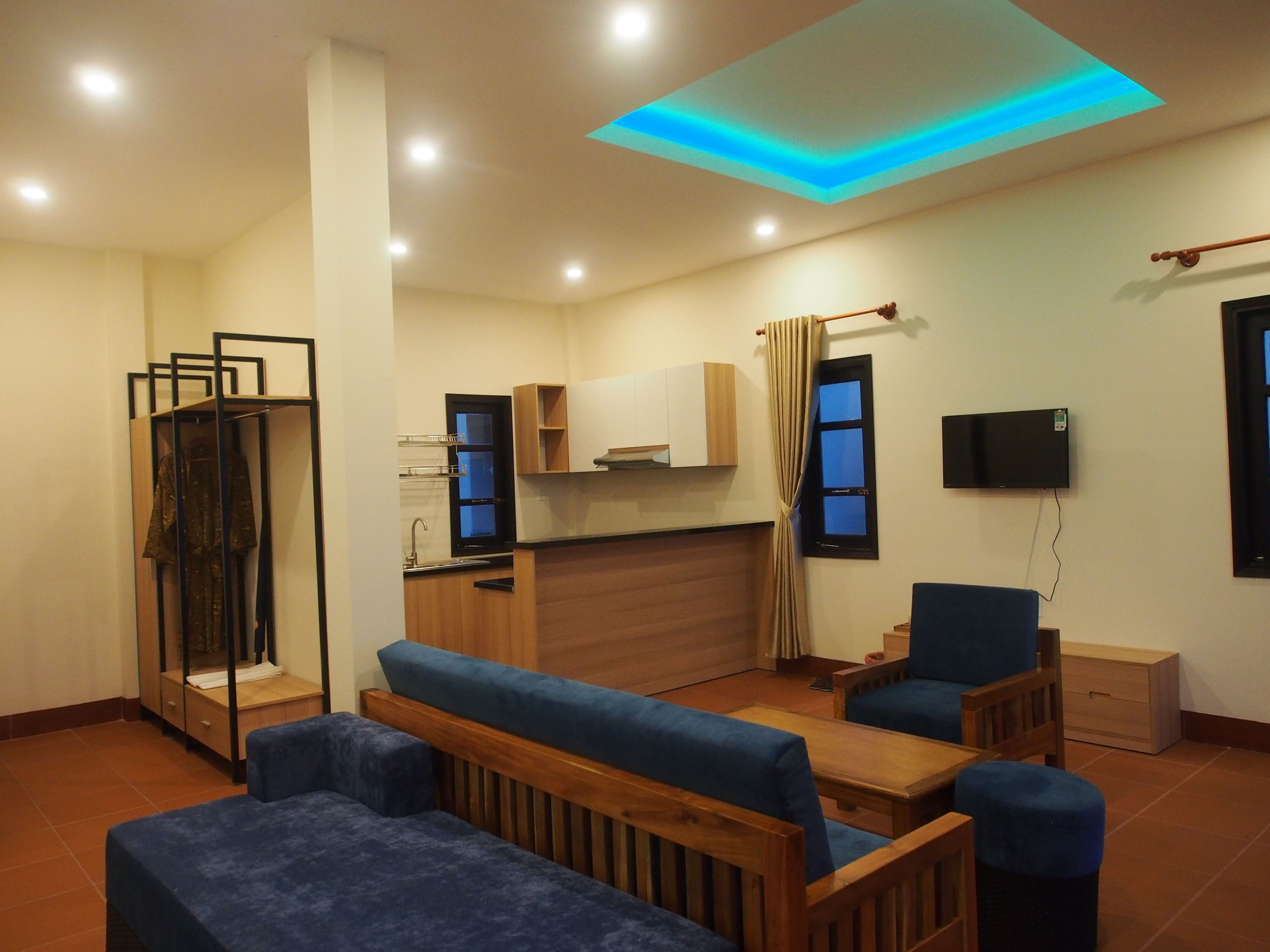 A compact living space with a kitchenette, a seating area with blue upholstered furniture, and a ceiling with a blue accent light.