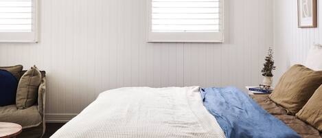 A bedroom with a bed, two windows, a sofa, and a small table.