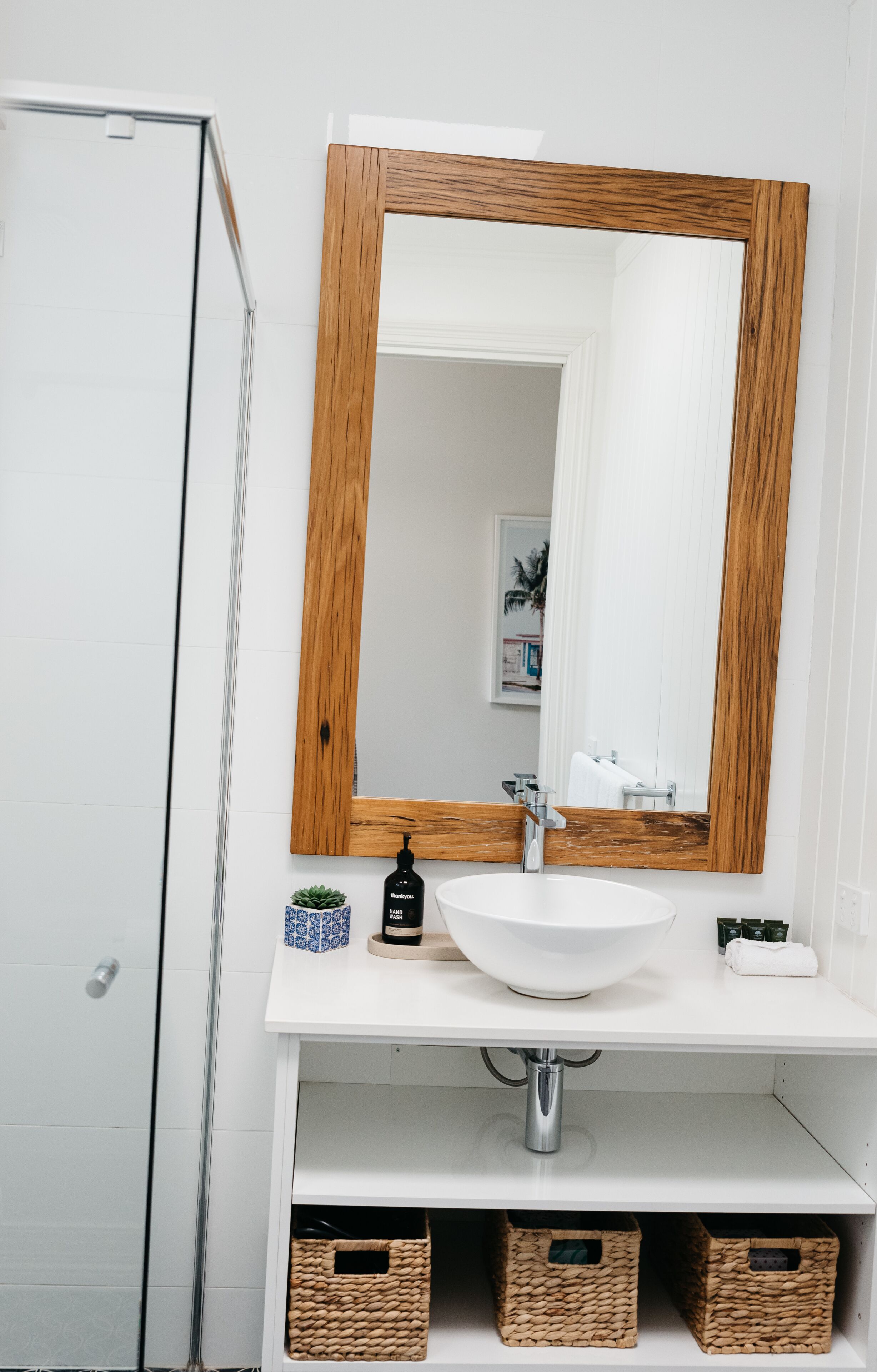 A bathroom with a white sink, wooden-framed mirror, and wicker baskets under the sink.