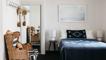A bedroom with a bed, a chair, a mirror, and a painting on the wall.