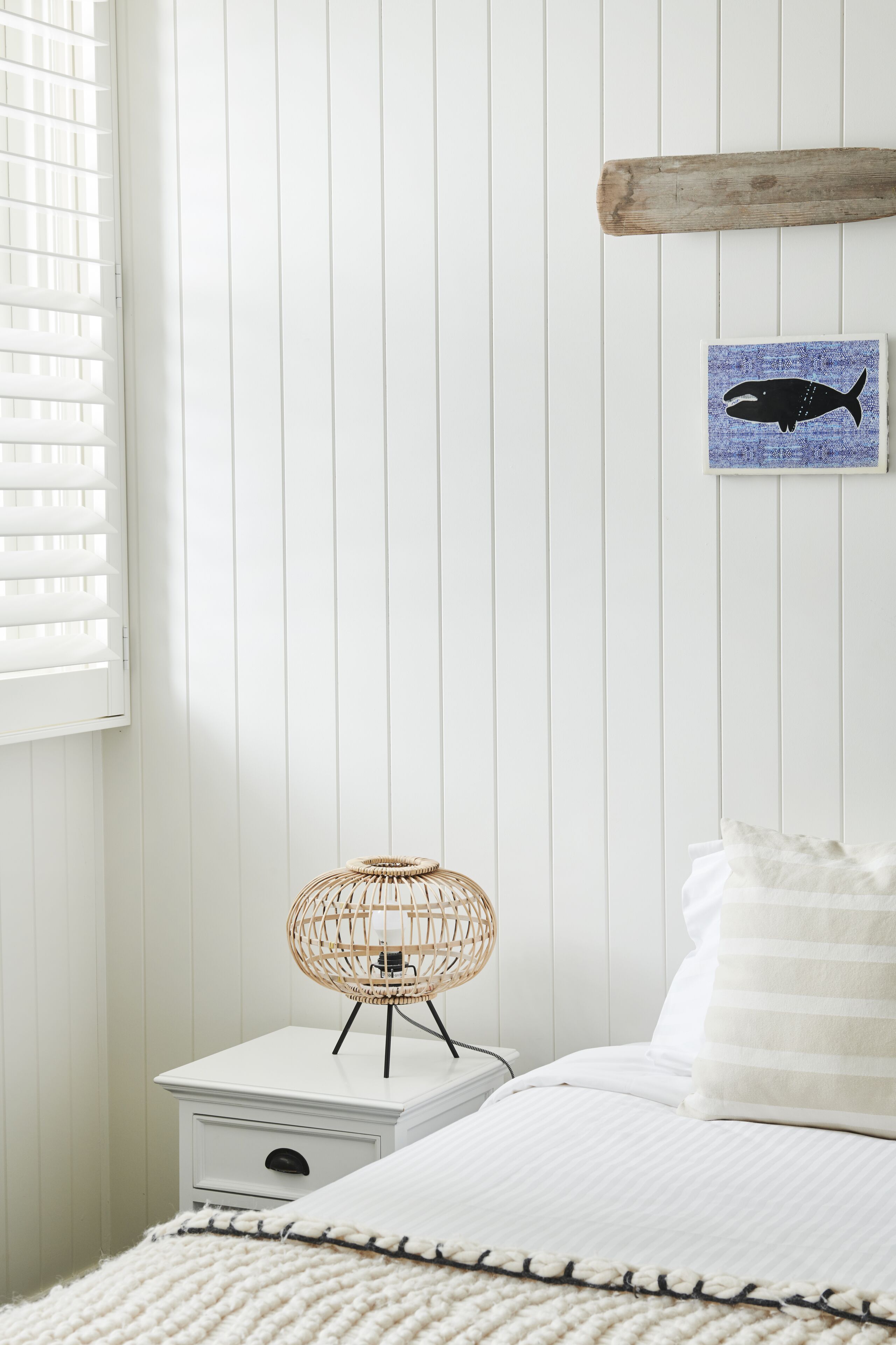 A bedroom with a bed, a nightstand, a wicker chair, a wooden beam, and a wall-mounted fish picture.