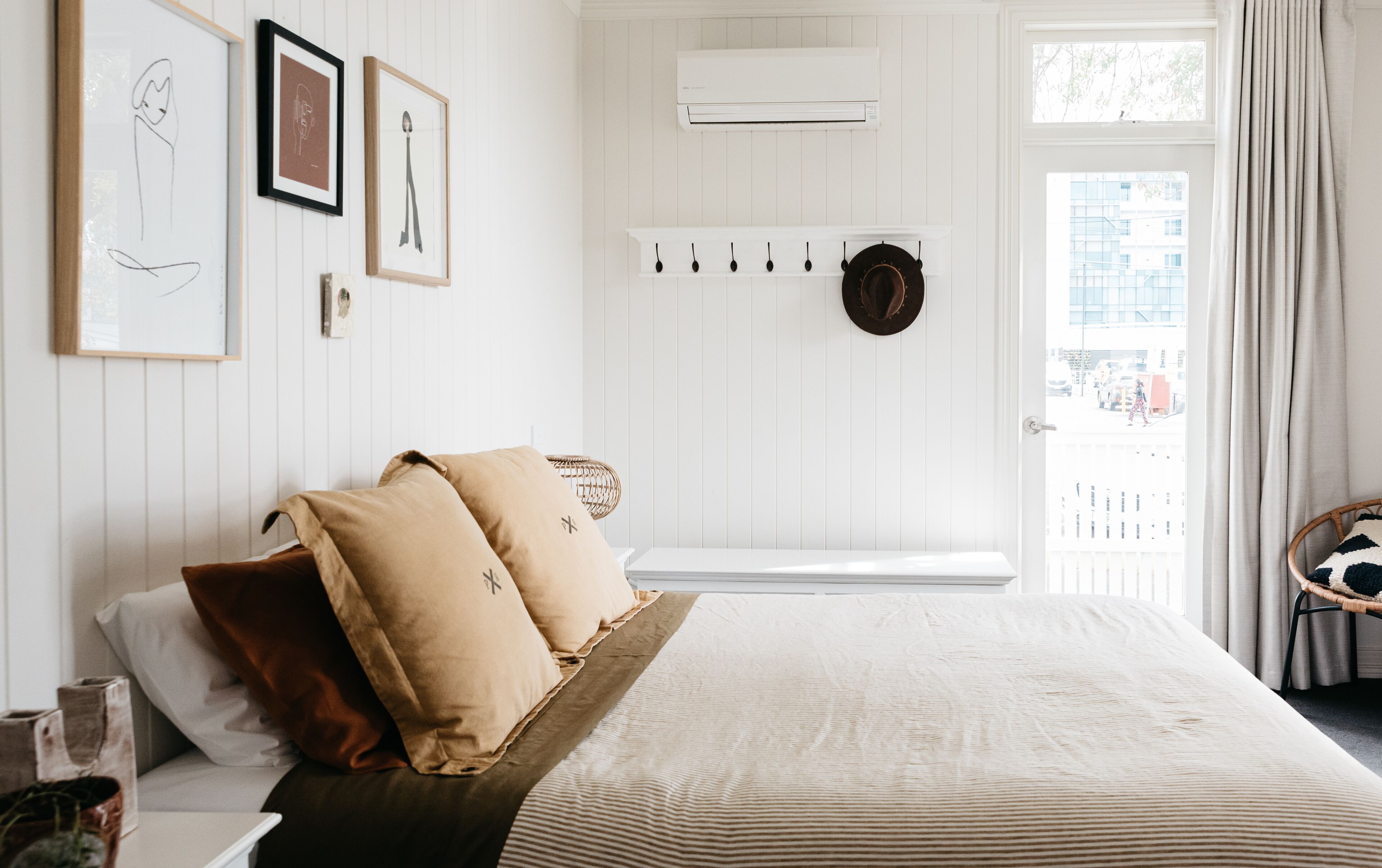 Una camera da letto con un letto, cuscini, un comodino, un condizionatore d'aria a parete e vista all'esterno.