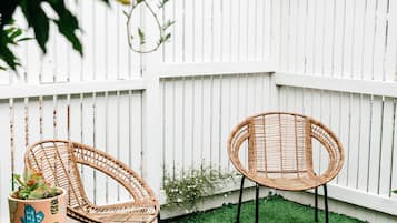 Two wicker chairs in a backyard with artificial grass, a wooden stump, and a potted plant.