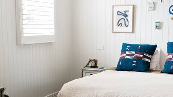 Une chambre à coucher avec un lit, une table ronde en bois, une fenêtre avec des stores et un tableau accroché au mur.