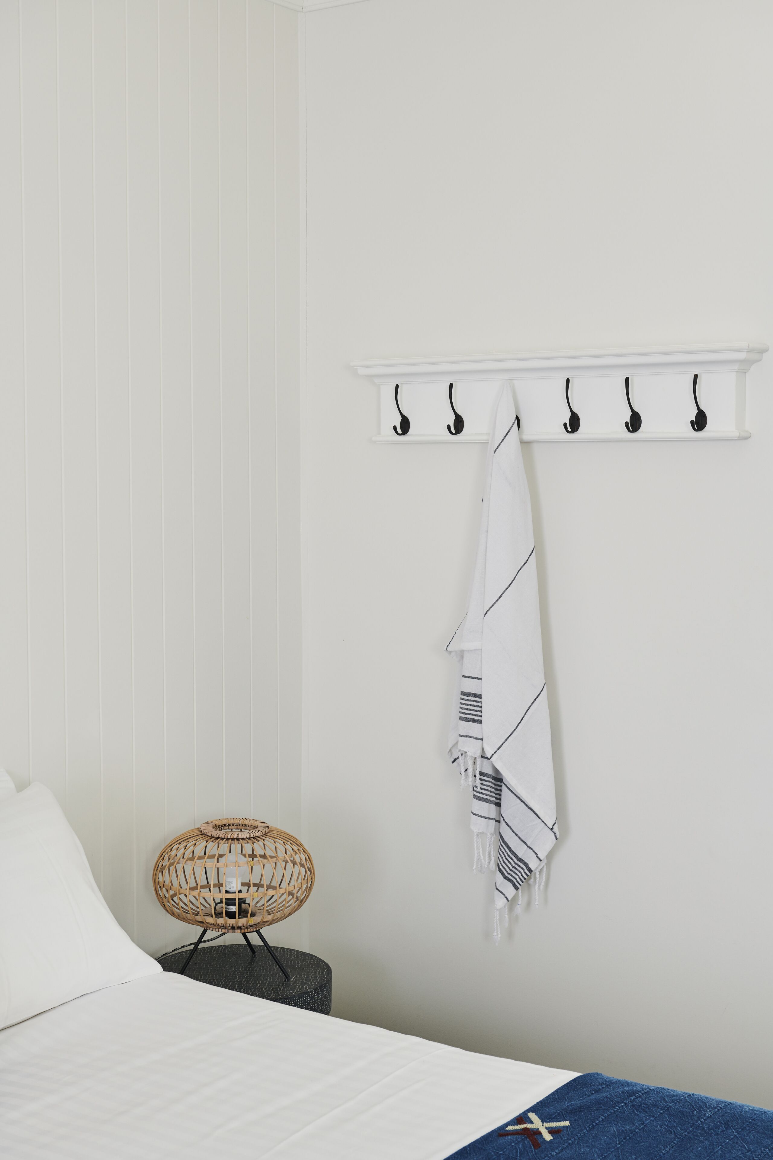 A bedroom with a bed, a chair, a wall-mounted towel rack, and a small round ottoman.