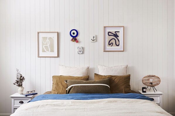 A neatly arranged bedroom with a bed, pillows, a nightstand, a vase with dried flowers, and two framed artworks on the wall. - Anchor Geelong (Geelong)