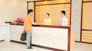 A reception desk with a patterned backdrop, a floral arrangement, and a man and two women standing in front.