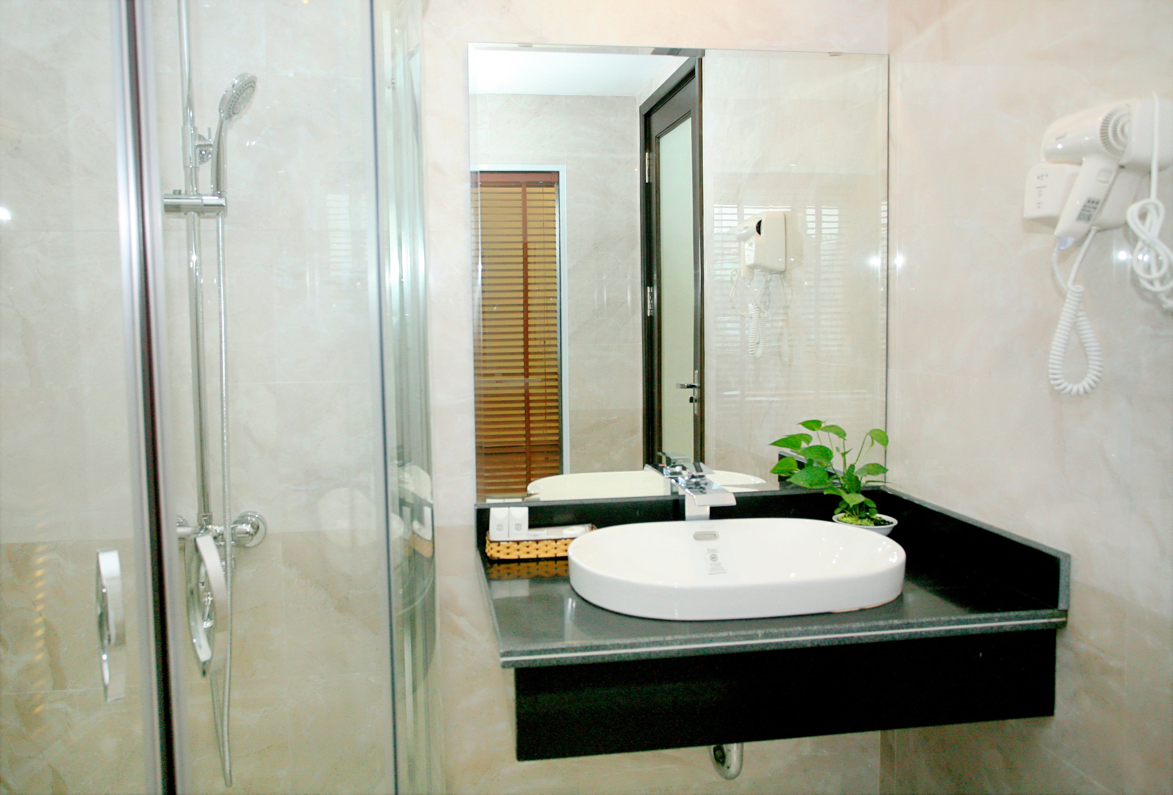 A bathroom with a glass shower enclosure, a sink with a mirror above it, and a hairdryer mounted on the wall.