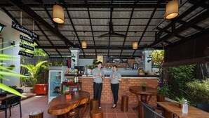 An outdoor cafe with wooden tables and chairs, a brick counter, and hanging lights. - Nika's House (Siem Reap)