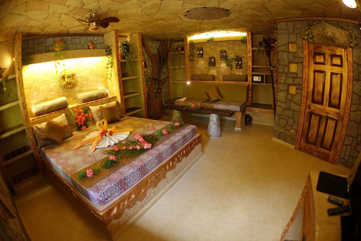 A cozy room with a large bed, a small seating area, and a stone wall.