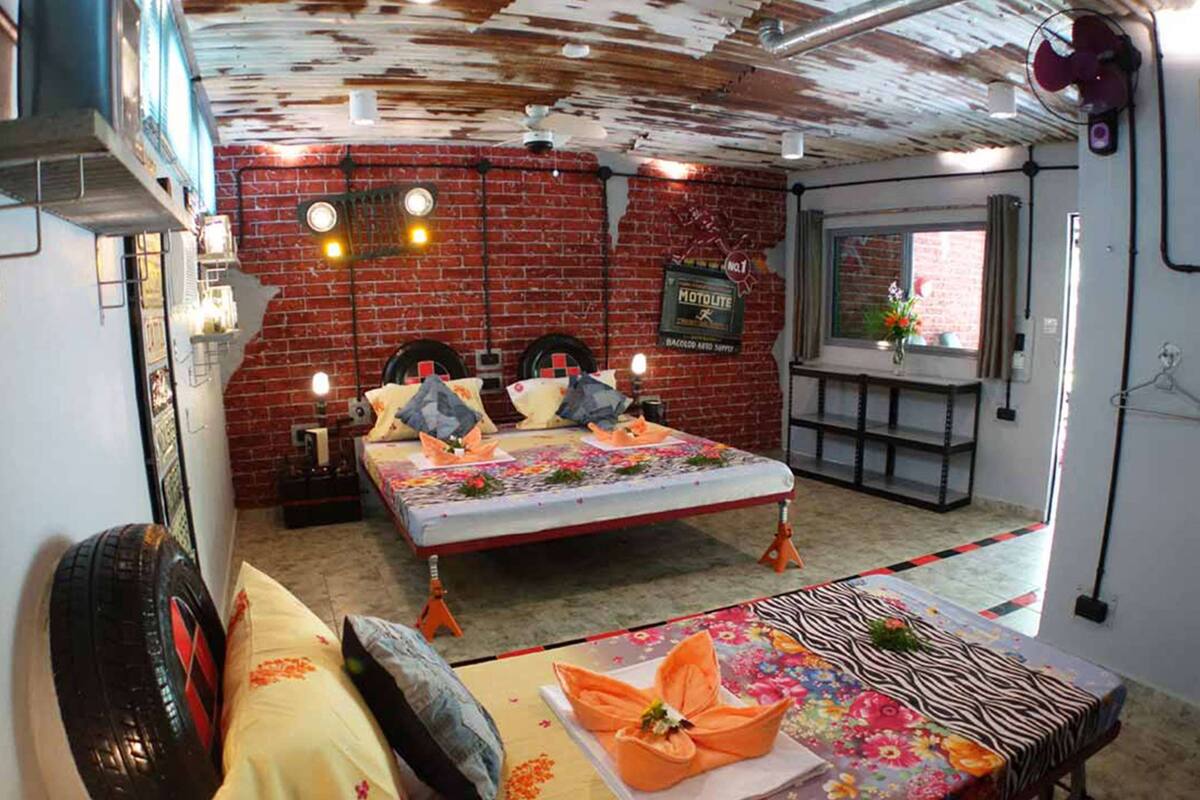 A room with a bed, a table with a floral tablecloth, and a brick wall with a sign.