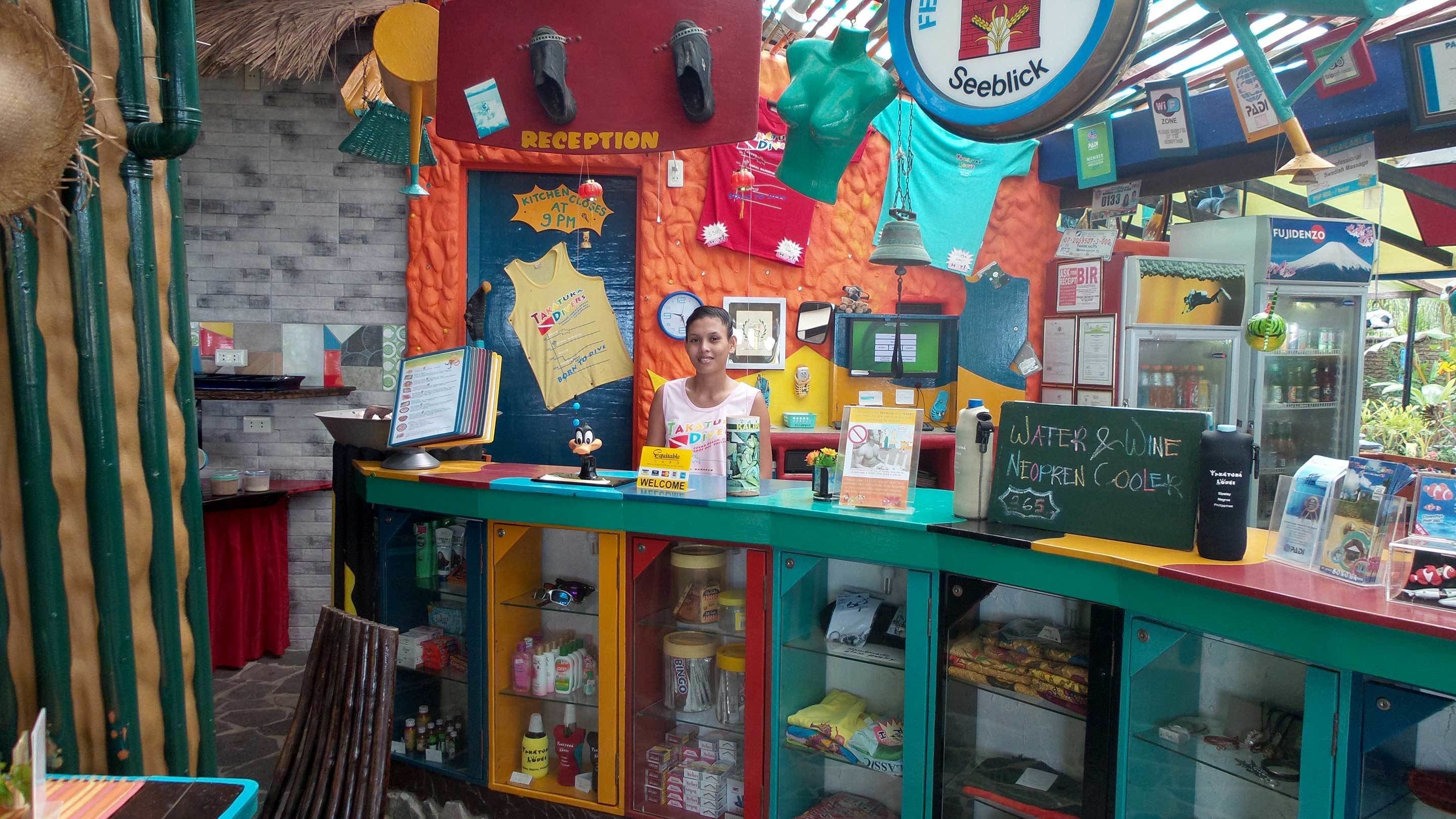 Un kiosque aux couleurs vives, comprenant un espace d’accueil, un ordinateur et divers articles exposés.