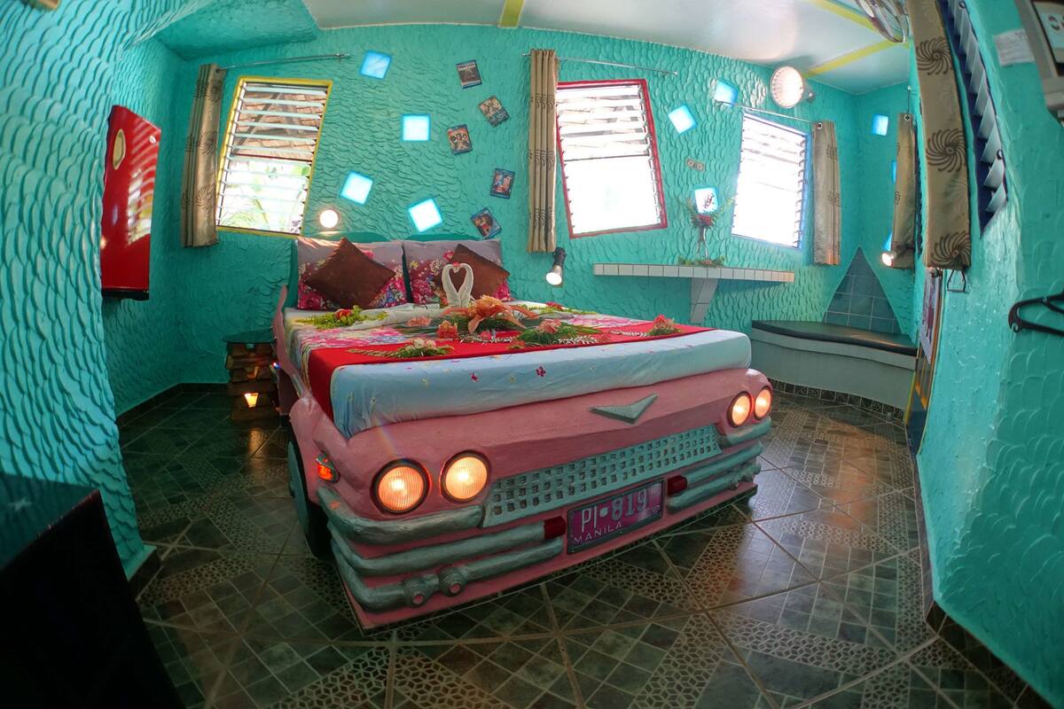 A uniquely designed bedroom with a car-shaped bed, a red refrigerator, and a tiled floor.