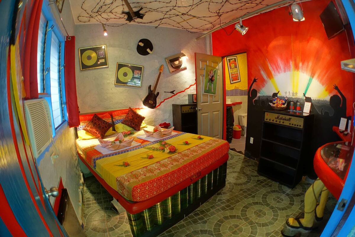 A room with a bed, a small table, a shelf, and a wall with decorations.