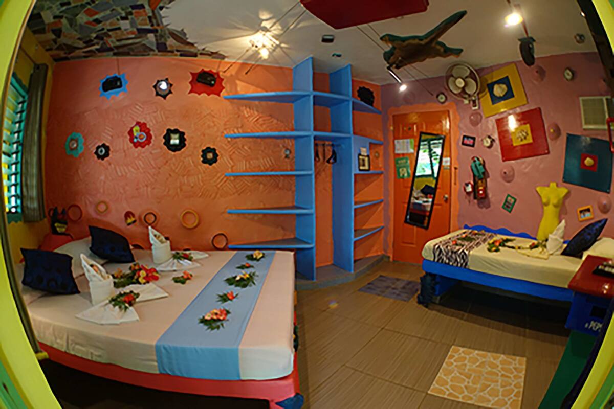A room with two beds, a blue shelving unit, and a ceiling fan.