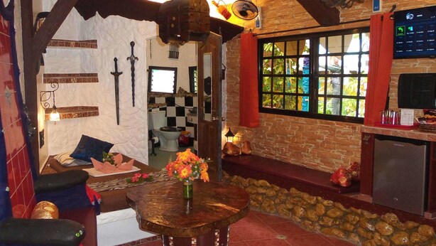 A rustic interior with exposed wooden beams, a stone wall, a stone bench, a wooden table with a vase of flowers, and a window with a view of greenery. - Takatuka Beach Resort (Sipalay)