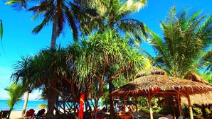 A beach scene with palm trees, a thatched-roof hut, and beach chairs. - Takatuka Beach Resort (Sipalay)