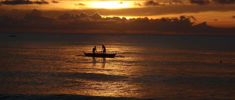 A sunset over a calm sea with a boat carrying two people.