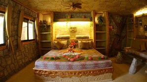 A bedroom with a stone wall, a bed with a patterned bedspread, and a ceiling fan. - Takatuka Beach Resort (Sipalay)