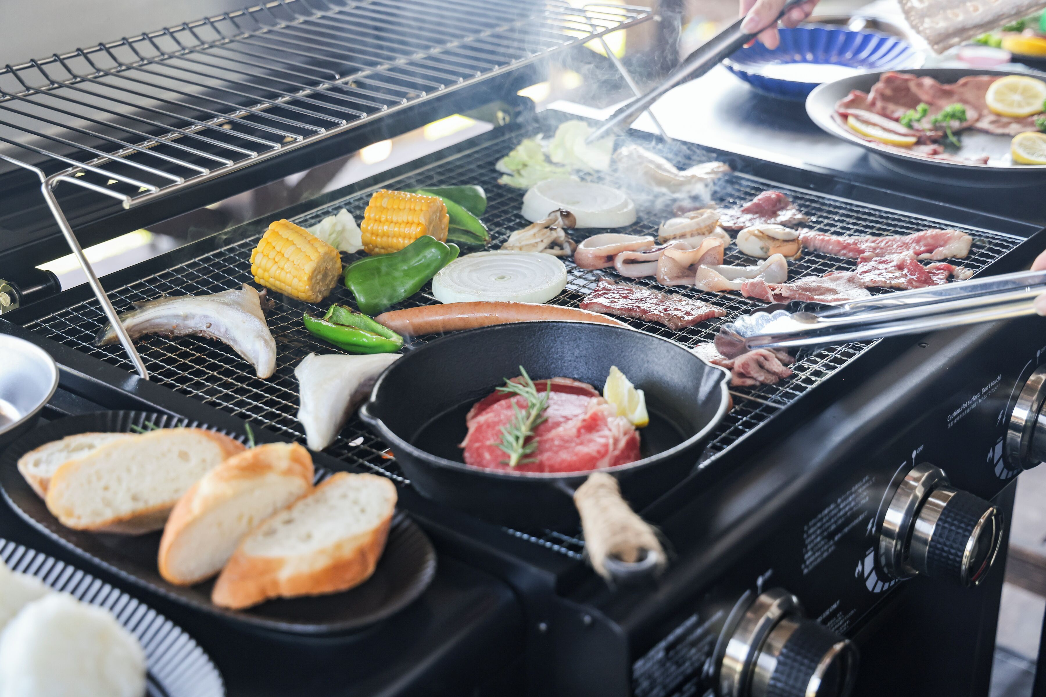 A grill with various meats, vegetables, and bread.