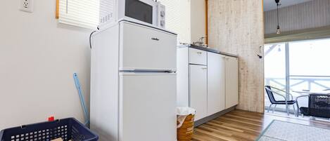 A compact kitchen with a microwave, refrigerator, and wooden flooring.