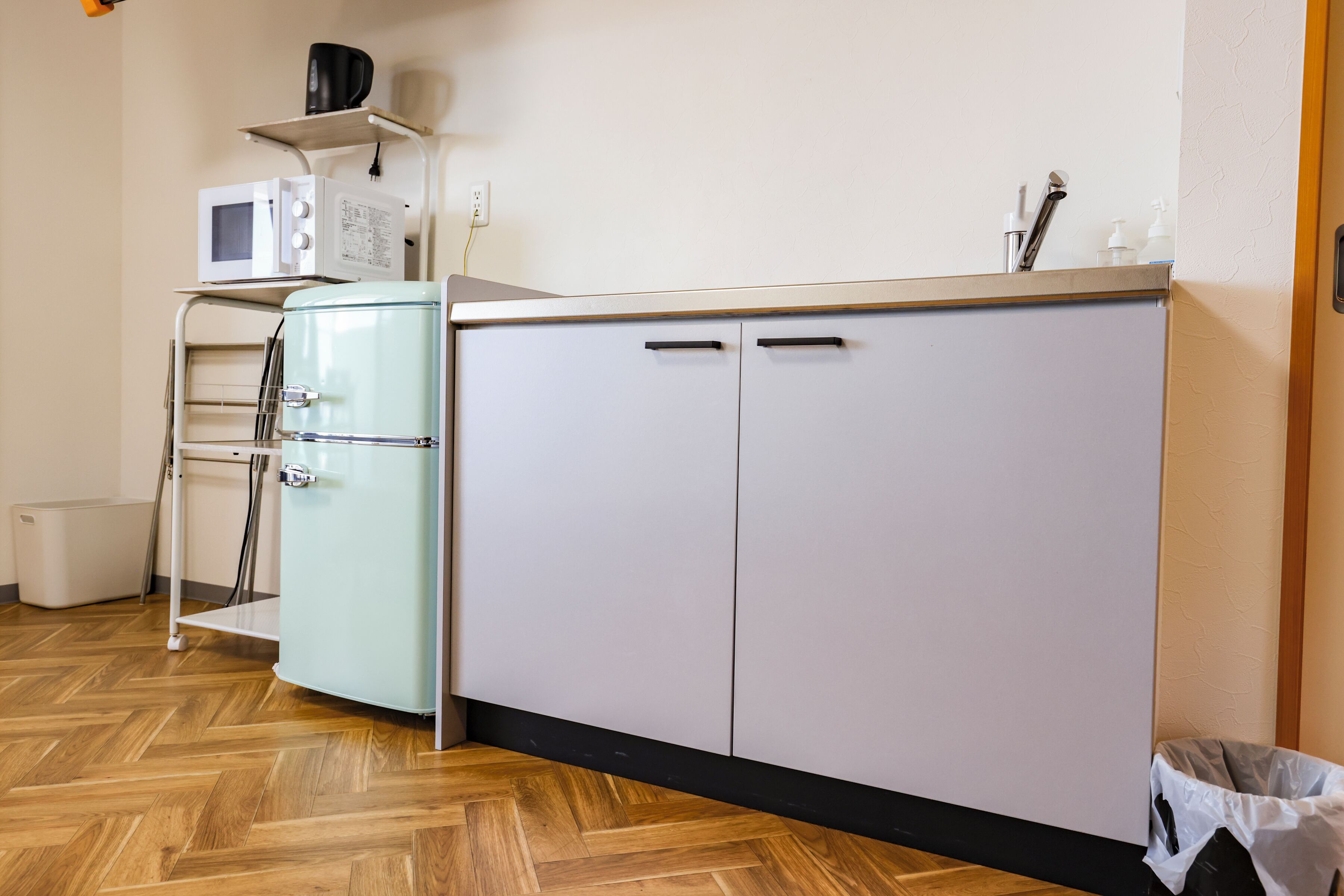 Eine Küchenzeile mit Mikrowelle, kleinem Kühlschrank, Spüle und Mülleimer.