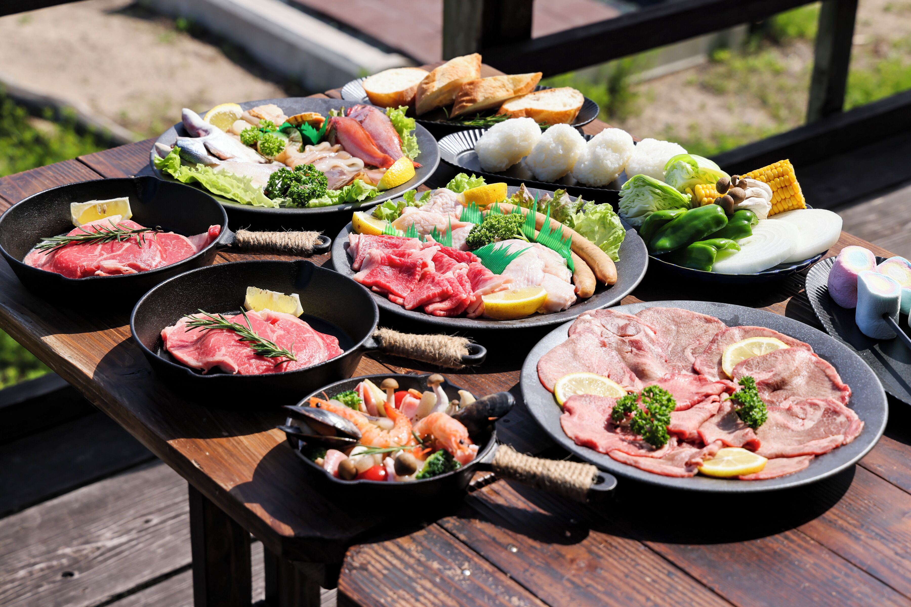 A variety of meats and vegetables on a wooden table outdoors.