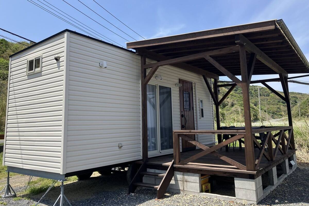 Une maison mobile dotée d’un porche et d’une petite porte, entourée de gravier et de végétation.
