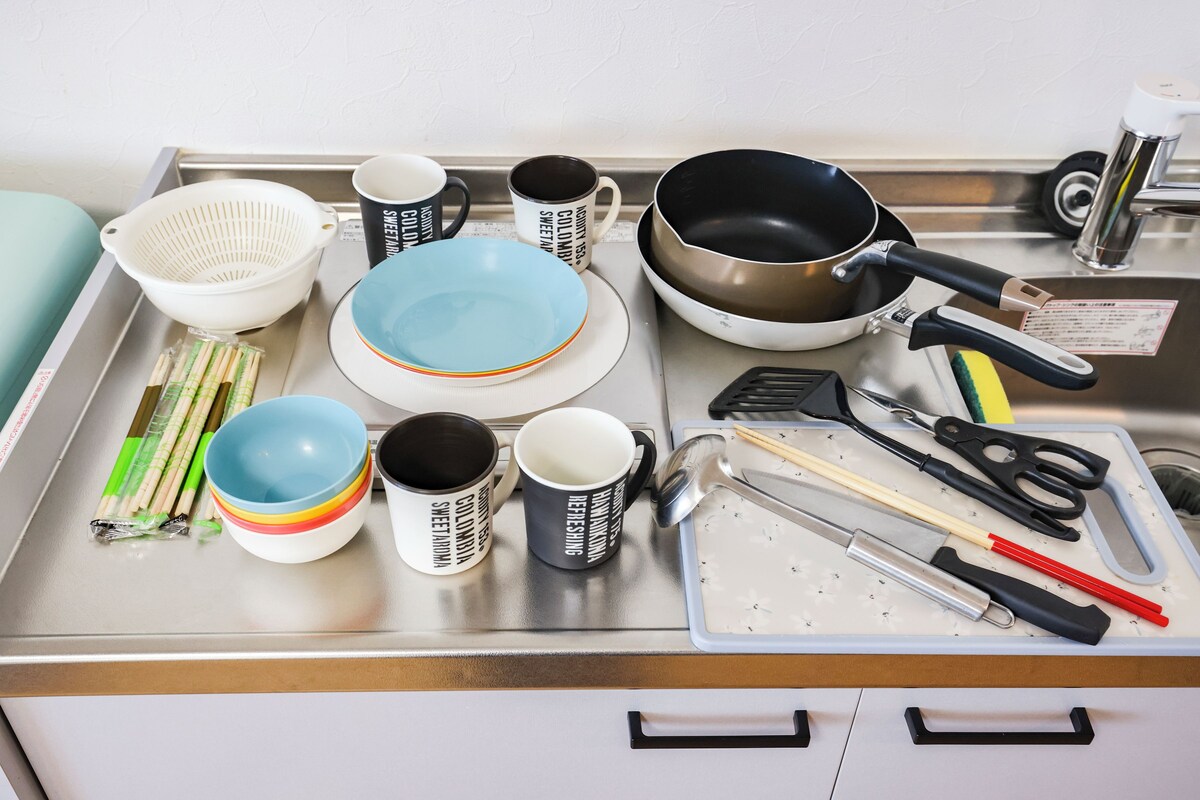 A kitchen counter with various utensils, a colander, plates, and mugs.