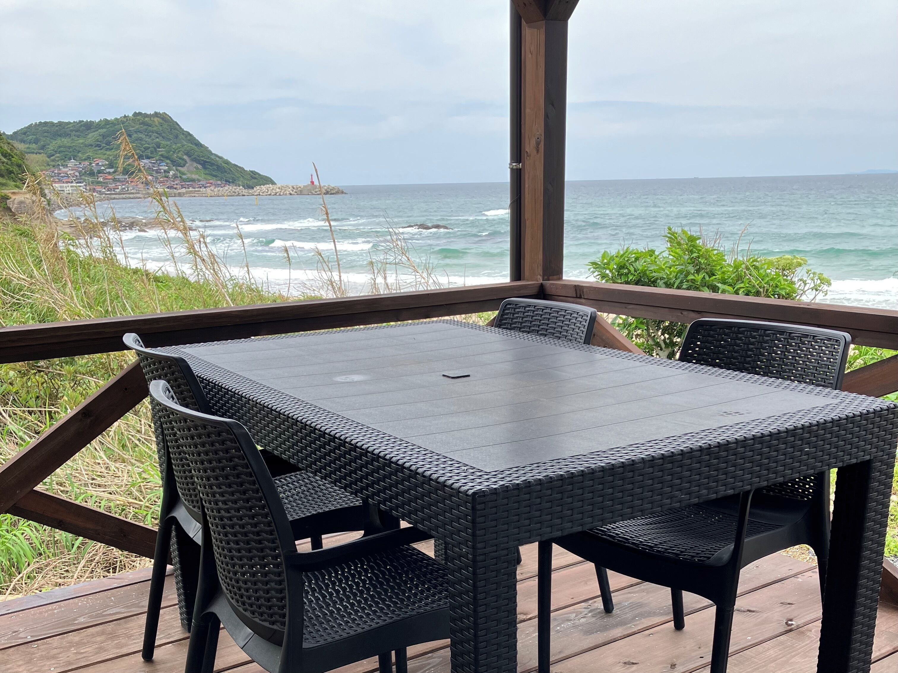 Eine Holzterrasse mit Tisch und Stühlen mit Blick auf den Ozean.