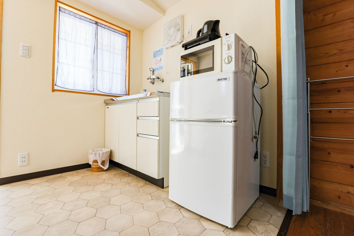 A kitchen with a refrigerator, a microwave, and a window with blinds.