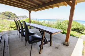 A covered outdoor dining area with a concrete floor, wooden table, and black chairs. - Sea Breeze 1987 (Nagato)