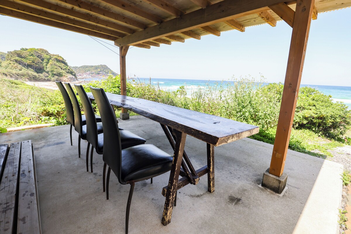 A covered outdoor dining area with a concrete floor, wooden table, and black chairs.