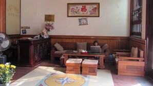 A traditional room with a wooden ceiling, a large framed artwork, a desk with a fan, and a seating area with a laptop. - Viet Nhat Halong Hotel (Bai Chay)