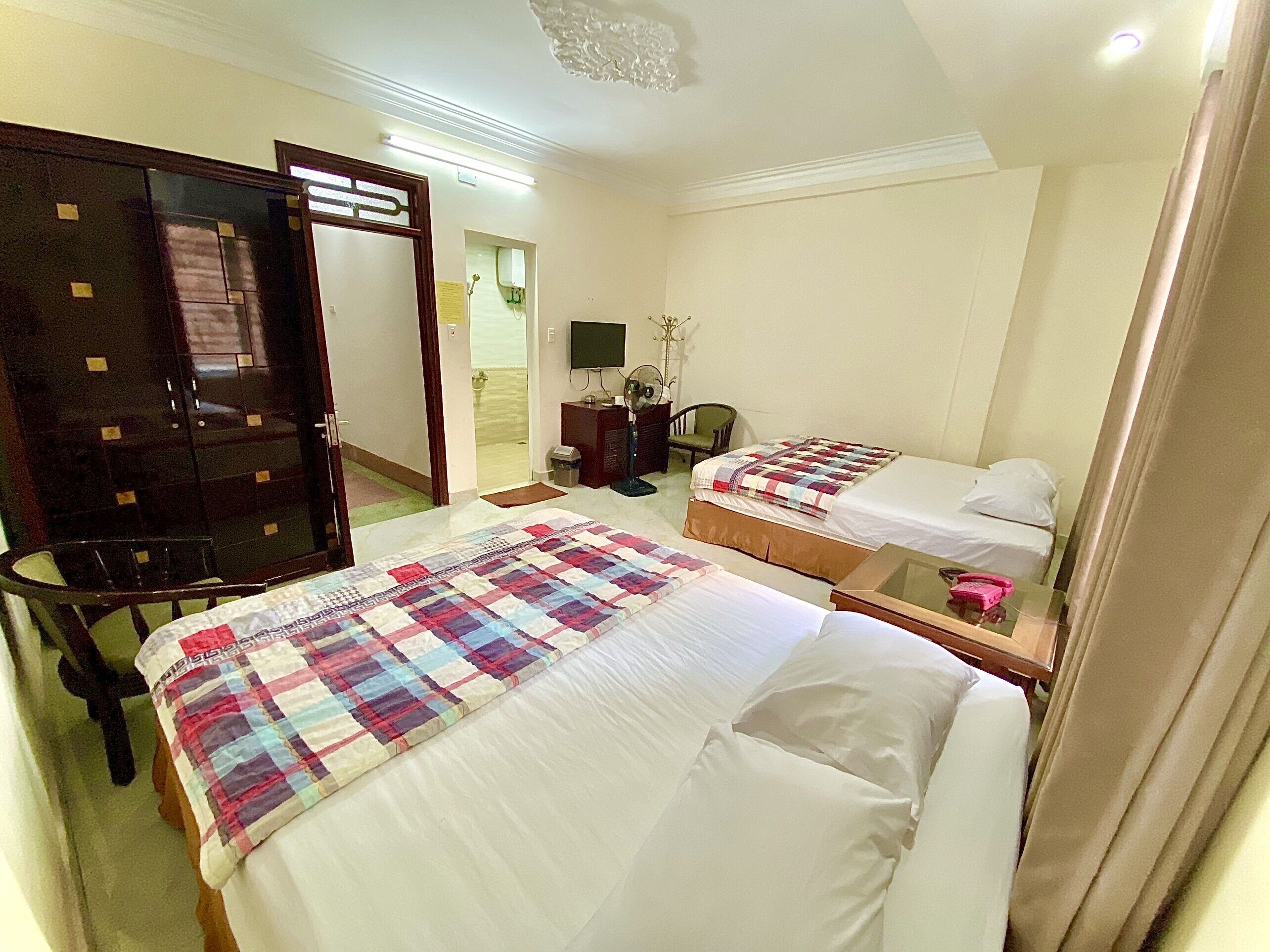 A hotel room with two beds, a desk, a chair, a television, and a door leading to a bathroom.