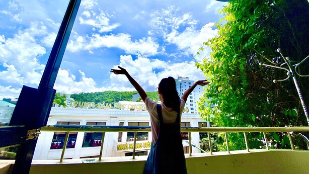 A person standing on a balcony with a view of a building and greenery. - Viet Nhat Halong Hotel (Bai Chay)